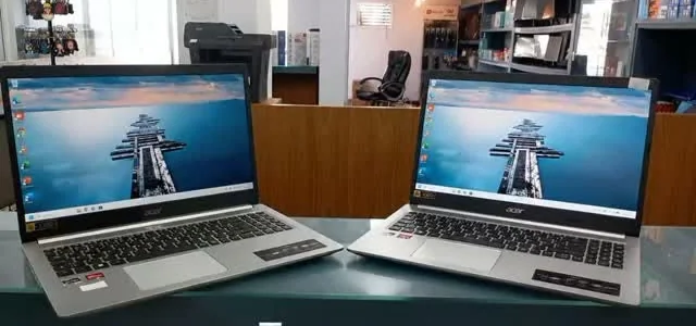 Dois notebooks abertos no balcão da Backup Informática, com as prateleiras de produtos ao fundo